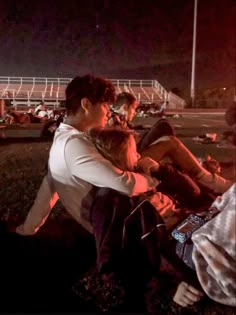 two people sitting next to each other on a field at night with the lights on