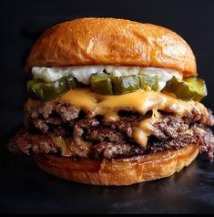 a cheeseburger with pickles and onions on a black surface, ready to be eaten