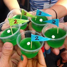 several people are holding cups with green liquid in them and one has a flag on it