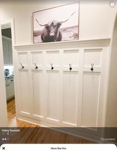 a white wall with some hooks on it and a cow photo hanging above the coat rack