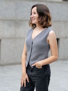 a woman standing in front of a building wearing a gray sweater and black jeans with her hands on her hips