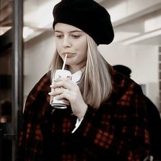 a woman with long blonde hair is drinking from a cup while wearing a black hat