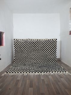 a black and white checkered blanket is on the floor in an empty room with wood floors