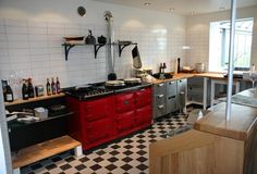 a kitchen with black and white checkered flooring, red stove top oven and cabinets