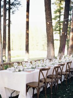 a long table with white linens is set up in the woods for an outdoor dinner