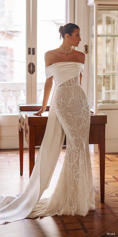 a woman in an off the shoulder wedding dress leaning on a table with her back to the camera