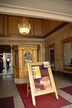 a sign in the middle of a room with red rugs on the floor and chandelier above it