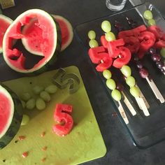 watermelon and grapes are arranged on a cutting board next to the knifes