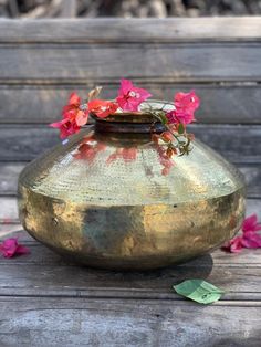 a vase filled with pink flowers sitting on top of a wooden table next to leaves