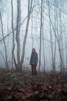 a woman standing in the middle of a forest on a foggy day with trees