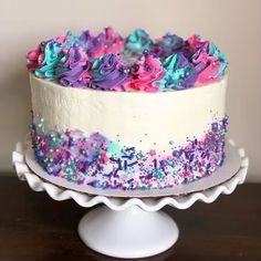 a white cake with sprinkles on it sitting on top of a wooden table