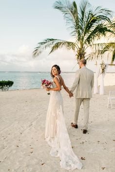 a bride and groom walking on the beach holding hands with palm trees in the background