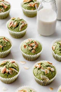 cupcakes with green frosting and almond toppings on a white surface next to a bottle of milk