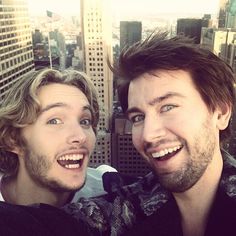 two young men standing next to each other in front of tall buildings and skyscrapers