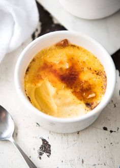 a white bowl filled with food sitting on top of a table next to a spoon