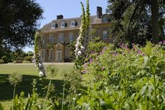 a large house sitting in the middle of a lush green field with lots of flowers