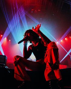 a man sitting on top of a stage with his hands in the air while holding a microphone