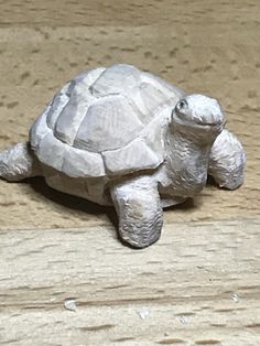 a small plastic turtle sitting on top of a wooden table next to a piece of wood