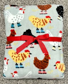 a gray blanket with chickens and roosters on it, tied to a red ribbon