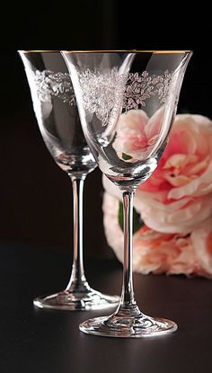 two wine glasses sitting next to each other on a black surface with flowers in the background