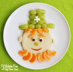 a white plate topped with an orange and grapes face