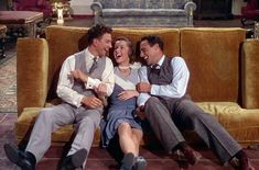 two men and a woman sitting on a couch with their arms around each other as they laugh