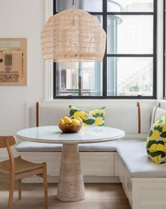 a white table and bench in a room with large windows, yellow pillows on the back