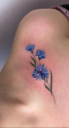 blue flowers on the back of a woman's left side rib - up tattoo