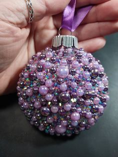 a hand holding a purple ornament that has been made with beads and ribbon