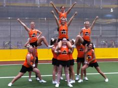 a group of girls in orange and black cheerleaders on a field with their hands up