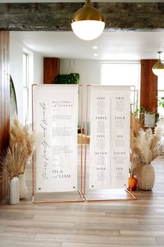 two white menu boards sitting on top of a wooden floor next to vases and plants