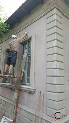 a man that is standing on a ladder in front of a building with a window