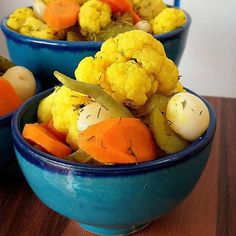 two blue bowls filled with vegetables on top of a wooden table next to carrots and cauliflower