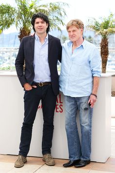 two men standing next to each other in front of a wall with palm trees on it