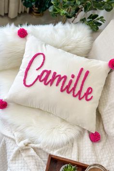 a white pillow with pink pom - poms on it that says,'camille '