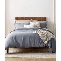 a bed with blue linens and pillows in a white walled room next to a wooden headboard