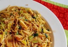 a white plate topped with noodles and veggies on top of a colorful table cloth