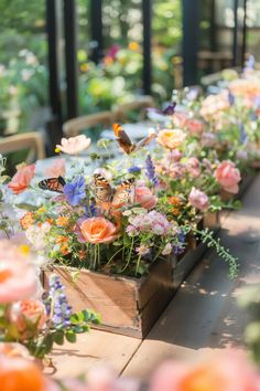 a long table with flowers and butterflies in wooden boxes on it's sides, along with other tables