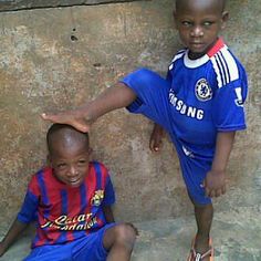 two young boys sitting next to each other in front of a stone wall and wearing blue uniforms