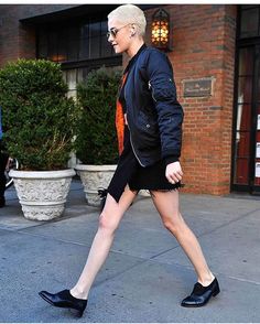 a woman walking down the street wearing black shoes and a jacket with zippers on it