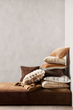 a pile of pillows sitting on top of a brown couch next to a white wall