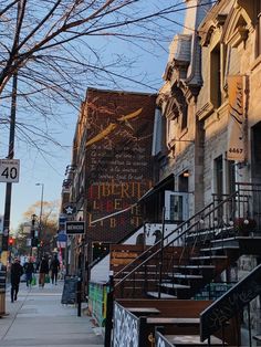 people are walking down the sidewalk in front of some buildings with stairs and signs on them