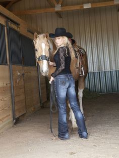 a woman standing next to a brown horse in a barn with another horse behind her