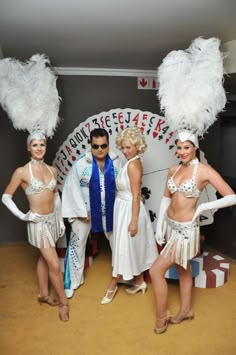 three women and two men in costumes posing for a photo with white feathers on their heads