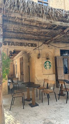 tables and chairs are set up outside an old building with thatched roof over the starbucks sign