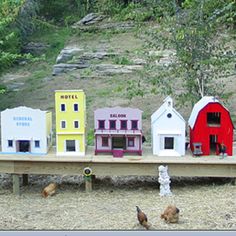 a group of small buildings sitting on top of a wooden table next to chickens and trees