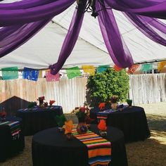 an outside area with tables covered in purple cloths and colorful decorations on the table