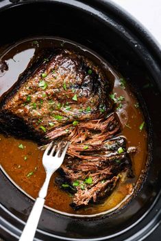 a pot filled with meat and gravy next to a fork