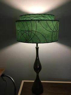 a green lamp sitting on top of a wooden table next to a wall with a white light