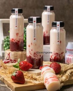 four bottles filled with liquid and strawberries on a table